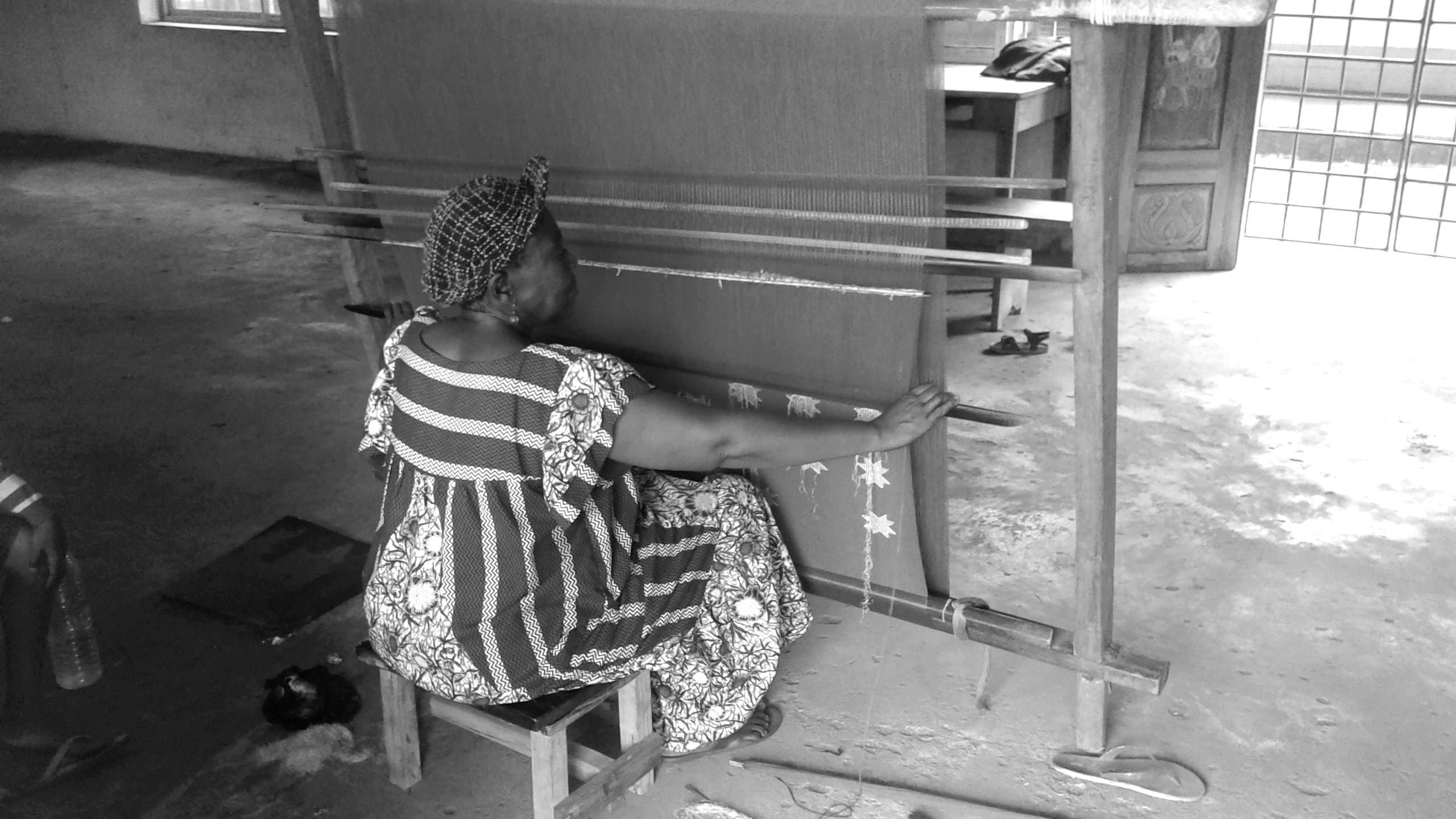 A Nigerian woman hand-weaving Akwete cloth on a traditional loom, Abia State. Monochrome.